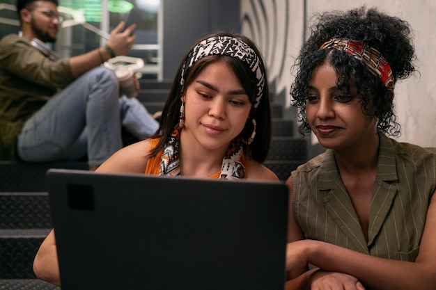A diverse group of Argentinian students collaborating on a coding project using laptops in a bustling classroom. The room is well-equipped with modern technology, reflecting an emphasis on digital literacy.
