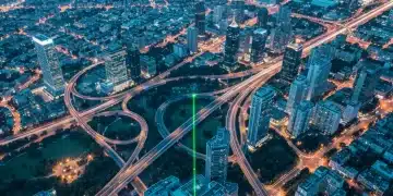 Vista aérea de uma cidade ao anoitecer com rodovias iluminadas e arranha-céus formando padrões geométricos complexos, representando a transformação digital.